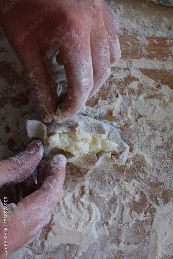 Obraz premium Stage of preparation of Karelian pies -Pirakka. Pies are located on a wooden board, being filled ready for baking. Dish of national cuisine - piirakka. Close-up.