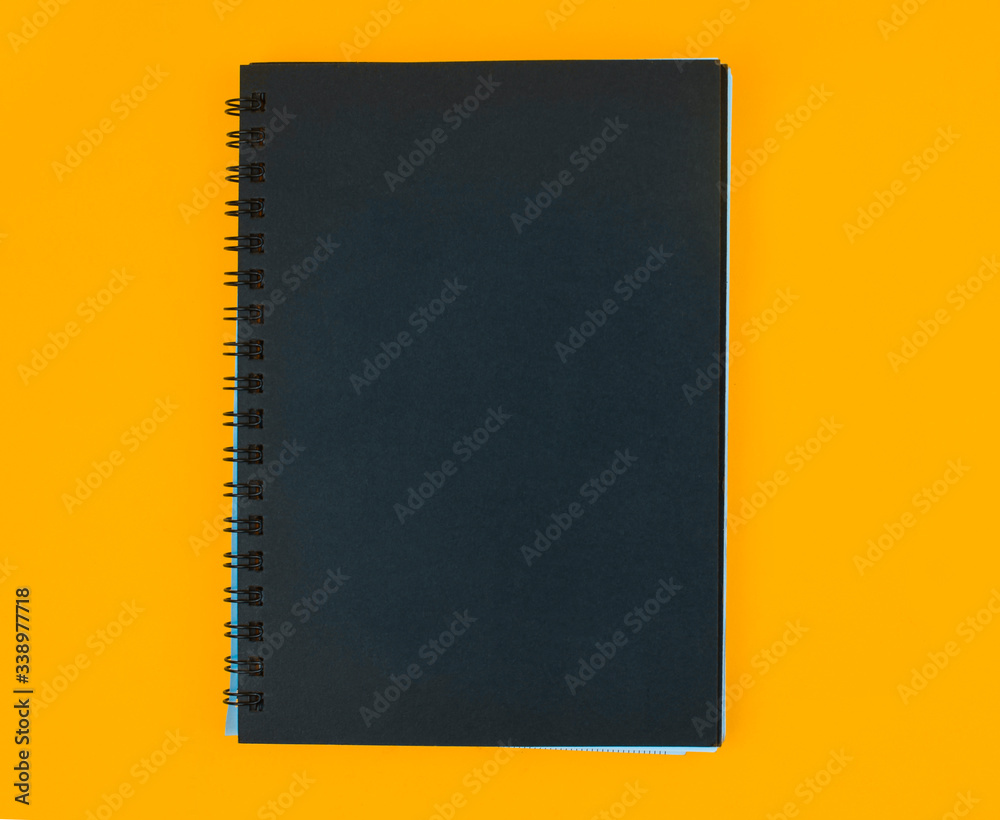 Fototapeta premium A diary of black color cover placed on an isolated orange paper background