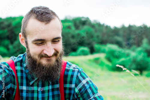 Handsome man hipster with beard on serious face in cloth shirt and suspenders sunny outdoor on mountain top against cloudy sky on natural. Tourism concept. Wonderful landscape.