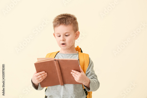 Surprised little boy reading book on color background