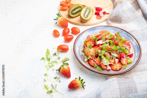 Vegetarian fruits and vegetables salad of strawberry, kiwi, tomatoes, microgreen sprouts on white concrete background. Side view, copy space.