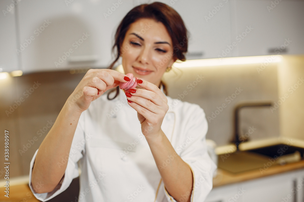 Confectioner in a kitchen. Woman in a uniform. Professional decorates the macaroni. Confectioner in a kitchen. Woman in a uniform. Professional decorates the macaroni.