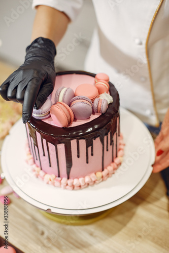 Confectioner in a kitchen. Woman in a uniform. Professional decorates the cake. photo