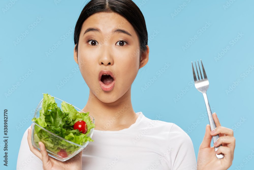 A woman of Asian appearance salad with eating blue background A woman of Asian appearance salad with eating blue background