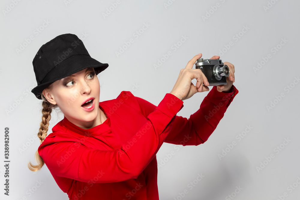 Youth Lifestyles. Funny Caucasian Blond Girl Posing With Old School Film Camera in Red Dress Against White.