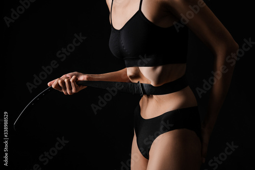Sick woman tightening her waist with belt on dark background. Concept of anorexia