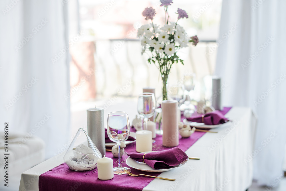 Festive table setting with marsala violet textile napkin and tablecloth, easter eggs, white dish and golden cutlery, candles and glass for wine. purple color