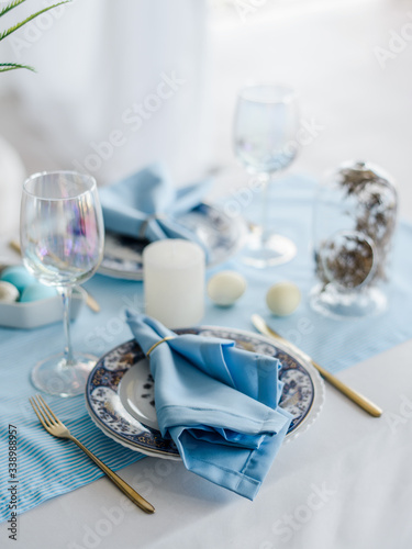 Holiday easter table setting with sky blue textile napkin and tablecloth, eggs, dish and cutlery, glass for wine. white home interior. Top view