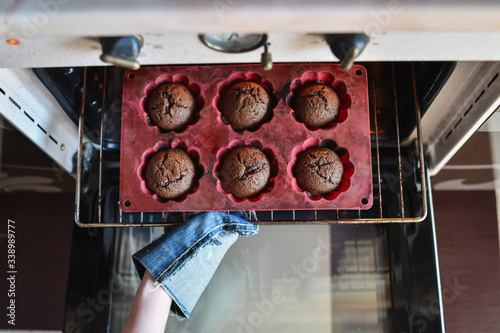 Top view of woman hands taking out freshlyy baked chocolate cup cakes or muffins out of hot oven. Selective focus.