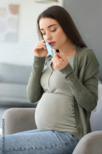 Pregnant woman putting on medical mask at home