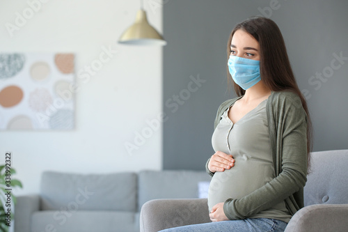 Pregnant woman wearing medical mask at home photo