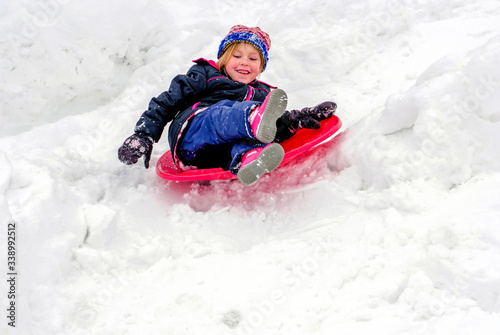 Laughing child sleds down a snowy hill on a red saucer sled 