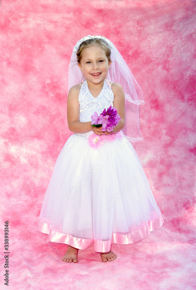 Little girl dressed as a  bride  poses on  a soft pink backdrop
