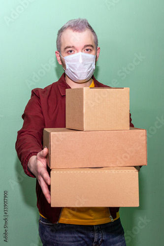 young delivery guy dressed in a yellow T-shirt, a dark red jacket and in a medical mask brought back several boxes, apartment view.