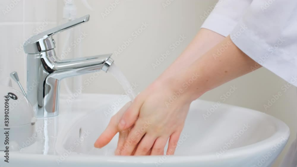 A woman doctor washes his hands in a sink under a stream of water, shakes them and turns off the water. Close up. Health care and prevention in hospital A woman doctor washes his hands in a sink under a stream of water, shakes them and turns off the water. Close up. Health care and prevention in hospital