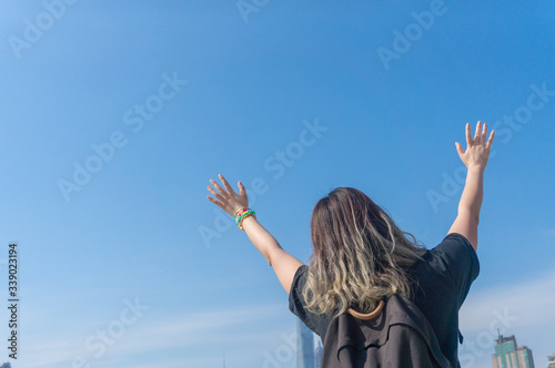 Asian girl traveller with dyed hair raises her hands and waving hands looking far away with the background of the Shanghai Lujiazui Cityscape and sky scrappers skyline in the sunny day