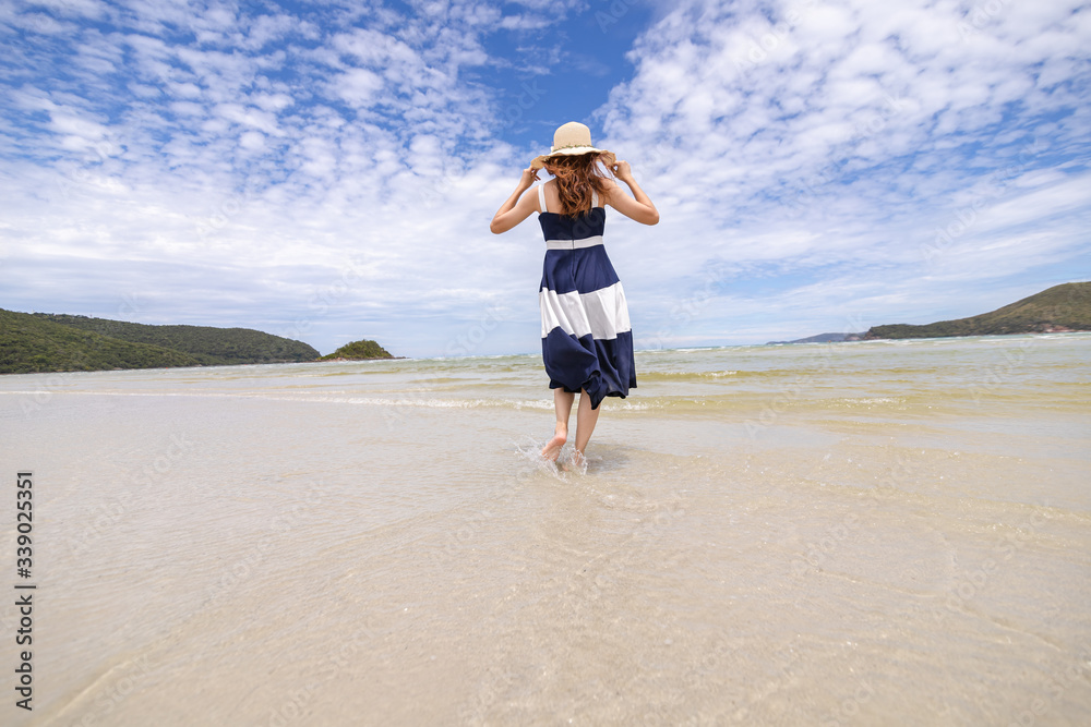Woman barefoot walking on summer along wave of sea water and sand on the beach.