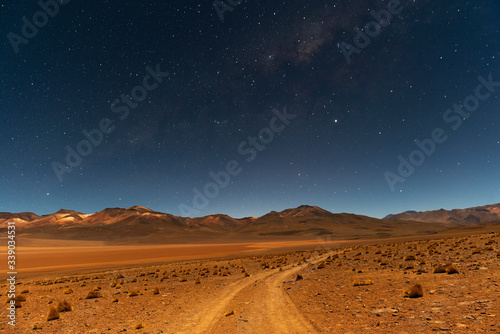 The Milky Way at night on the road in the Siloli Desert with the Andes mountain peaks in the background, Uyuni Salt Flat region, Bolivia. 