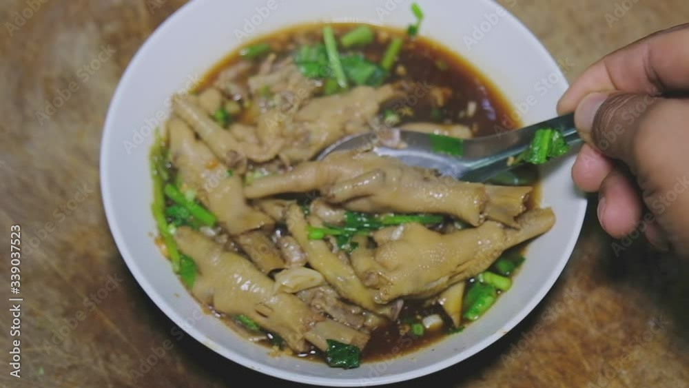 Slow motion hand using spoon holding thai style Chicken Feet Spicy herbal Soup  and smoke in white bowl on wooden table in restaurant.