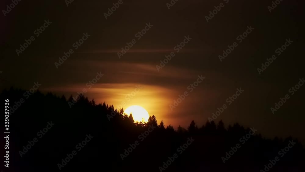 Epic time lapse of rising full moon silhouetted by a distant black forest, orange hazy glowing clouds Epic time lapse of rising full moon silhouetted by a distant black forest, orange hazy glowing clouds