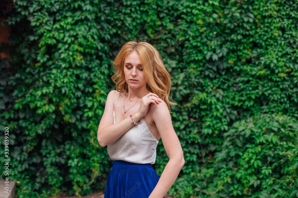 Portrait of a young beautiful woman, standing next to the wall of wild grape leaves holding a strap of a blouse. Portrait of a young beautiful woman, standing next to the wall of wild grape leaves holding a strap of a blouse.