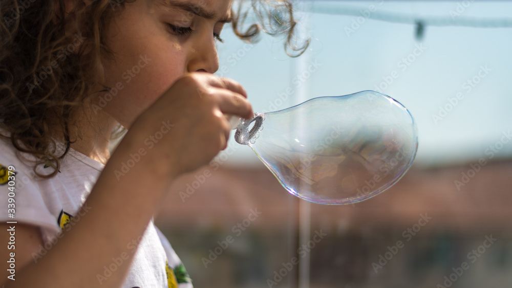 Isolated close up of a young girl during quarantine from the Corona Virus having fun on the balcony blowing soap bubbles- Israel Isolated close up of a young girl during quarantine from the Corona Virus having fun on the balcony blowing soap bubbles- Israel