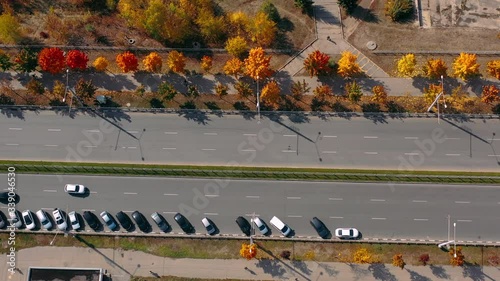 Aerial shot of driving cars on avenue with autumn trees on good asphalt . Top view of road traffic and parked cars in sunny weather in fall season in Kharkov, Ukraine. People go to work in cars.