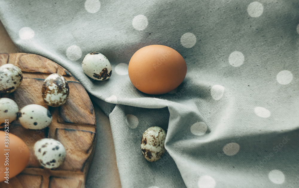 Chicken and quail eggs on a wooden board, next to a gray polka dot fabric; gray tint