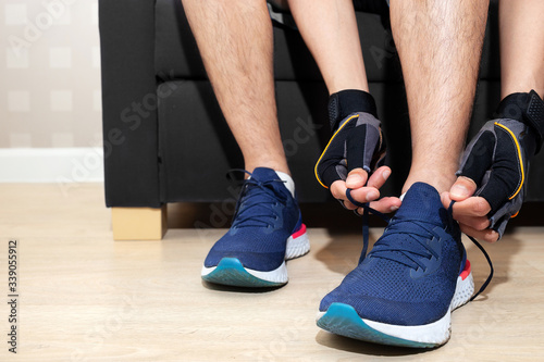 happy sport man tie shoelace of his running shoe on sofa in home living room for running  jogging  and exercise in fitroom and race running track for good health during work from home period