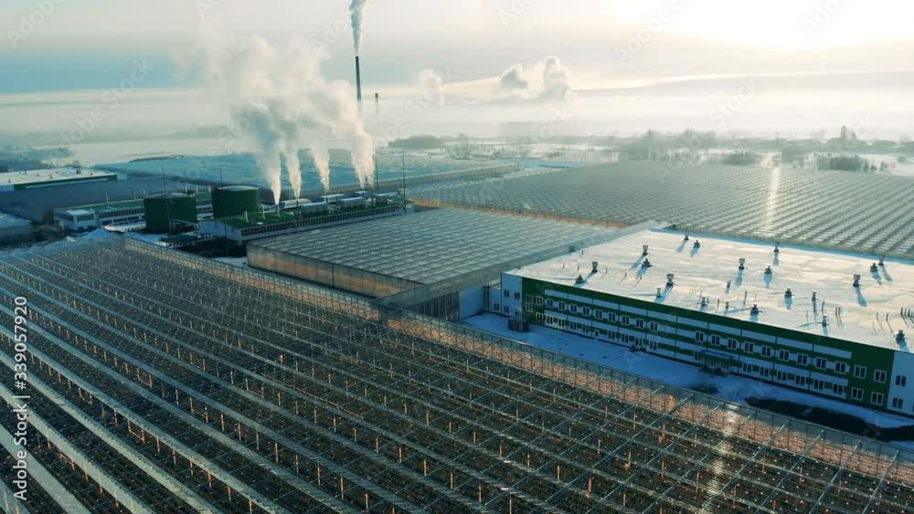 Outdoors view of glasshouse facilities with billowing chimneys. Power factory from above, steam from a smokestack.