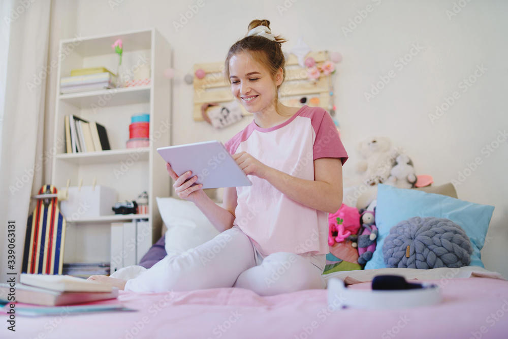 Young girl with tablet sitting on bed, relaxing during quarantine.