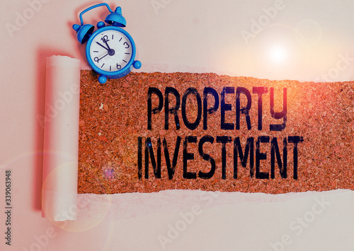 Writing note showing Property Investment. Business concept for Asset purchased and held primarily for its future income Alarm clock and torn cardboard on a wooden classic table backdrop photo