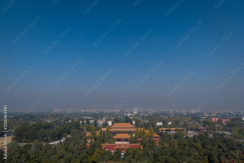 Scenic view overlooking the city of Beijing from Jingshan Park Palace gardens with temples, houses, rooftops and hazey blue sky in the background.