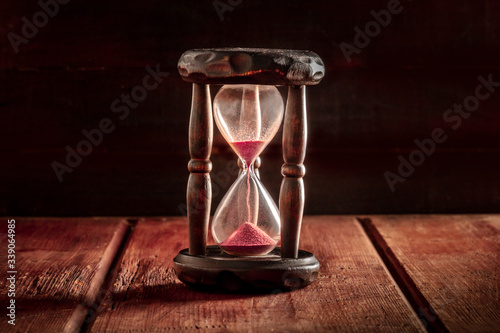 Time concept. An hourglass with sand falling through, on a dark rustic wooden background with a place for text