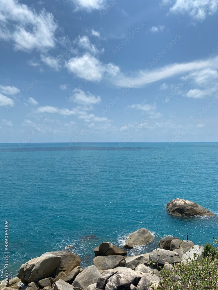 ocean, big rocks against the background of blue sky and white clouds on a tropical island in summer