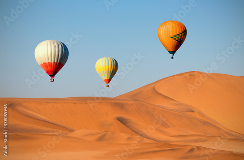 Colored hot air balloons flying over the sand dunes at sunset © Yuliia Lakeienko