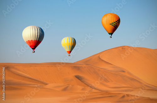 Colored hot air balloons flying over the sand dunes at sunset