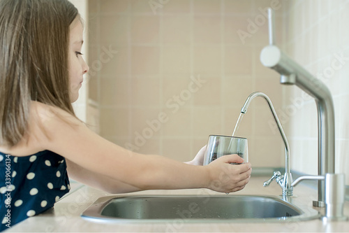 Girl using filter to purify drinking clean water. Kitchen faucet. Filling cup beverage. Infection viruses through tap water. Quality check. World water monitoring day. Environmental pollution concept