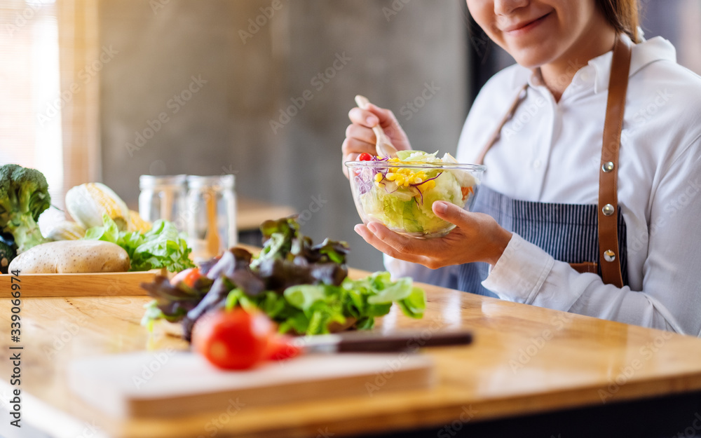 Closeup image of a beautiful female chef cooking and holding a bowl of fresh mixed vegetables salad to eat in kitchen