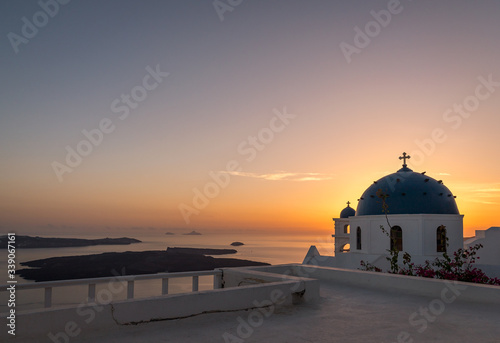 A beautiful sunset over the Caldera in Santorini overlooking two iconic blue dome churches in Imerovigli