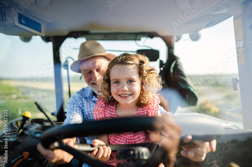 Obraz na płótnie Senior farmer with small granddaughter sitting in tractor, driving