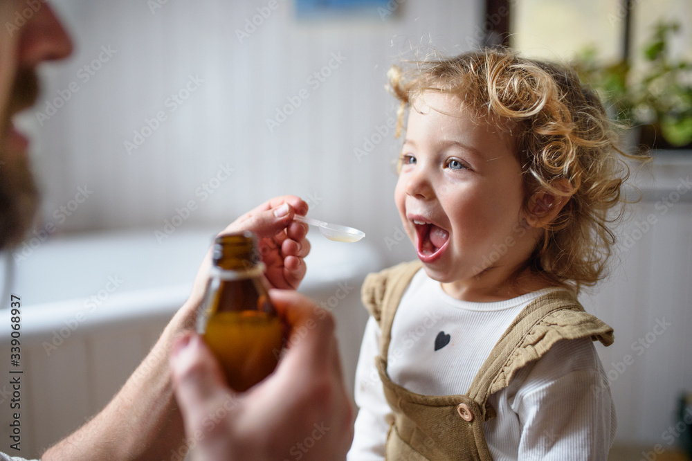 Unrecognizable father giving syrup to small sick daughter indoors at home. Unrecognizable father giving syrup to small sick daughter indoors at home.