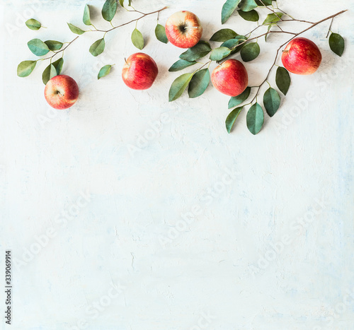 Tasty ripe red apples with branches and green leaves on rustic white background, top view. Border or frame with copy space for your design