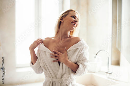 Beautiful woman enjoying in hotel. Young happy women in bathrobe use the cream for the body.	