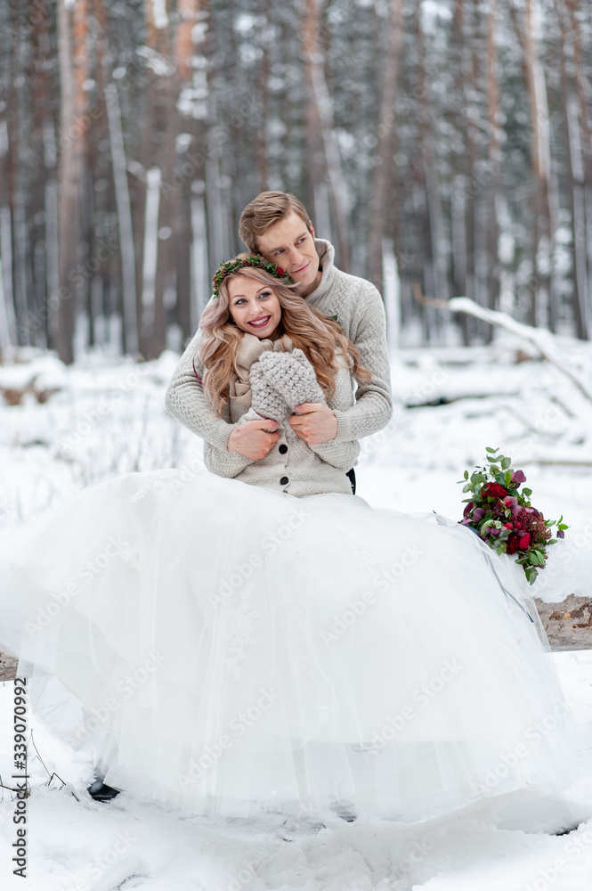Cute couple in love with a bouquet are sitting on the log on background of the winter forest. Artwork. Winter wedding. Copy space Cute couple in love with a bouquet are sitting on the log on background of the winter forest. Artwork. Winter wedding. Copy space