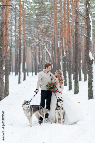 Cheerful couple are playing with siberian husky in snowy forest. Winter wedding.
