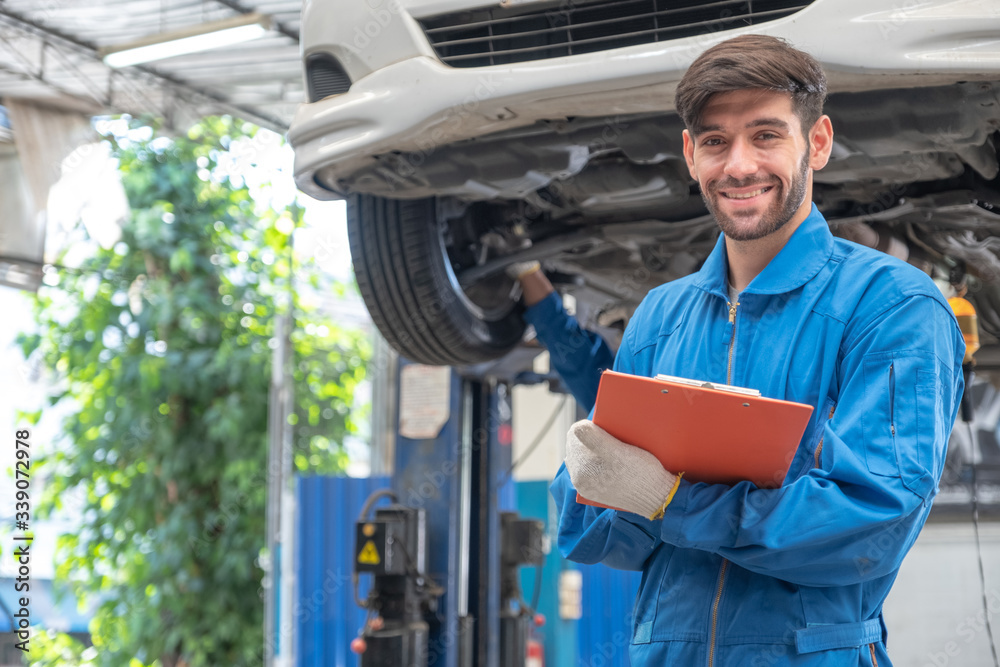 Professional mechanic worker holding clipboard and smiling in front of car lifting.