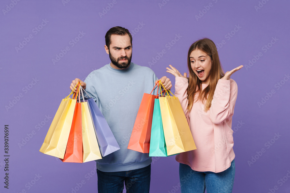 Girl near displeased boyfriend holding shopping bags.