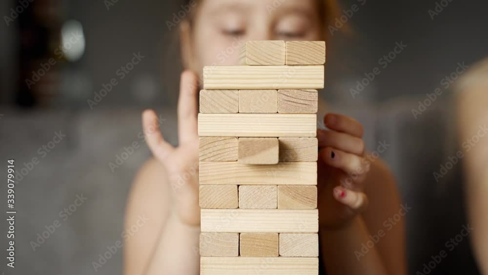 Games at home: A beautiful girl plays with her cute daughter in the jenga tower. They are sitting on the couch in the living room. The girls are laughing and smiling. Child makes her move. Slow motion