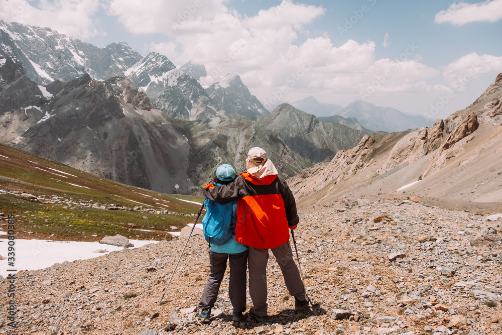 Tajikistan. Fann mountains Summer. A pair of elderly people in sportswear are hugging and looking at the high mountains. Love. Elderly people and sports (activity, hiking)